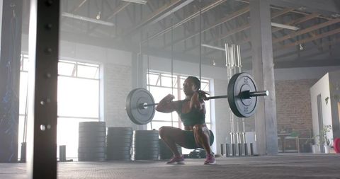 Woman performing loaded front squat in industrial warehouse gym, lifting heavy barbell