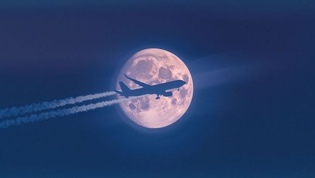Silhouetted commercial jet passing full moon at twilight
