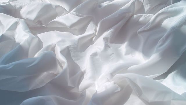 Gentle ripples of white bedsheet illuminated by natural light