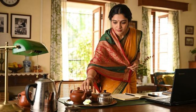 Indian woman in mustard saree reaching for clay teapot while working at home desk
