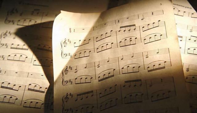 Vintage sheet music pages curling on wooden desk with warm sunlight and musical notation