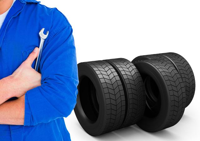 This image shows a mechanic in a blue uniform holding a wrench with two tires in the background. It is ideal for use in automotive repair advertisements, car service promotions, maintenance guides, and professional mechanic services marketing materials.