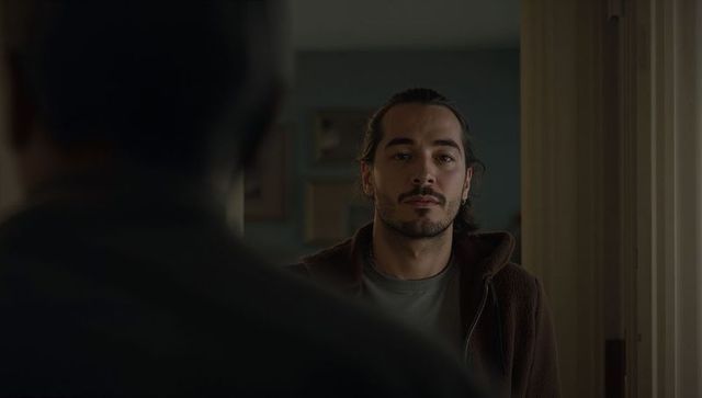 Moody young man standing in doorway wearing zip-up jacket and earring, introspective portrait