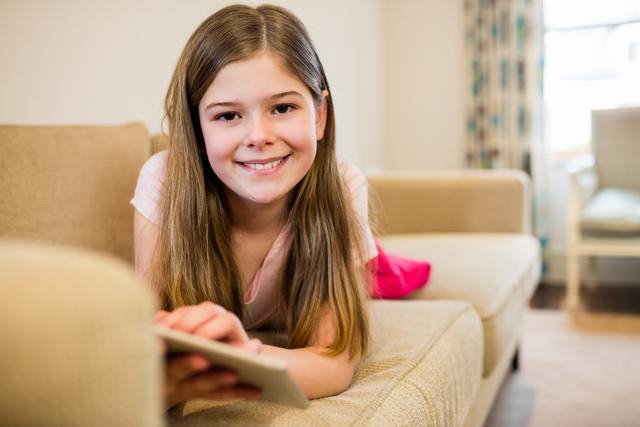 Portrait of girl lying on sofa using digital tablet in living room at home