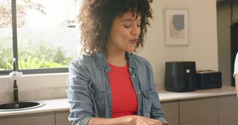 African american woman preparing meal at kitchen counter in red top and denim shirt