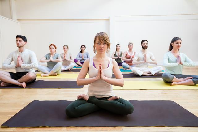 Trainer assisting group of people with lotus position