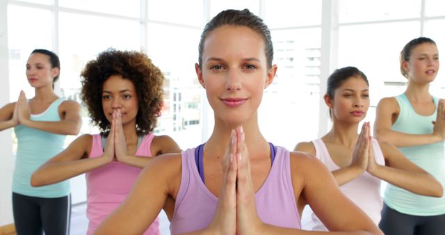 Diverse women in a bright studio are practicing yoga together, each holding a prayer pose. Suitable for promoting yoga classes, fitness studios, group meditation sessions, and wellness retreats. Emphasizes themes of mindfulness, healthy lifestyle, and diverse fitness environments.