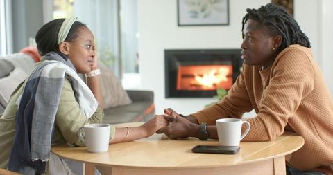 African-american couple holding hands sharing heartfelt conversation by cozy fireplace