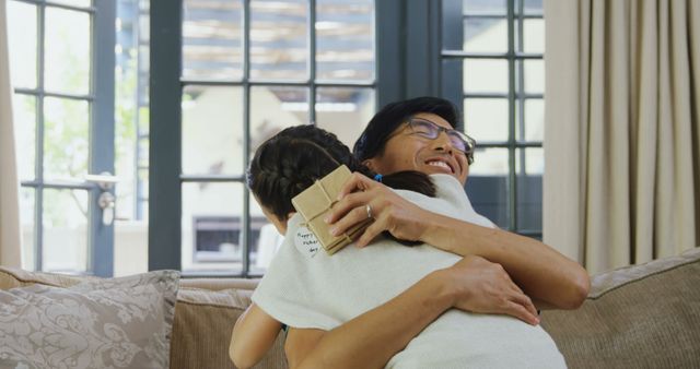A middle-aged Asian woman embraces a child, with copy space. Their warm hug in a cozy living room setting conveys a sense of love and familial affection.