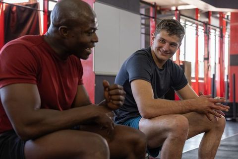 Gym partners resting, planning next set, smiling and chatting, post-workout camaraderie