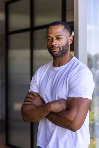 Confident african-american executive leaning in modern sunlit entryway wearing white tee