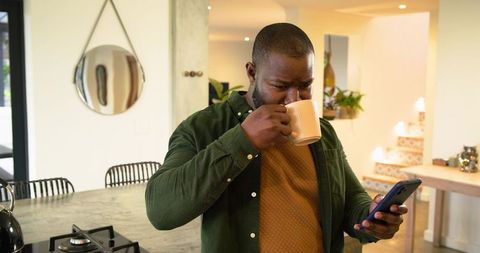 African American man sipping mug and checking smartphone in modern open-plan kitchen