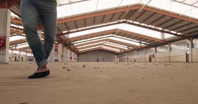 Caucasian male ballet dancer practicing ballet moves in an empty warehouse. His legs and feet are the main focus as he gracefully turns on the dusty floor. This stock video can be used for content involving dance, art practice, creativity, industrial settings, and artistic expressions in unusual locations.