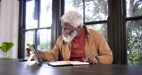 Senior man using tablet at wooden table for study and work in peaceful environment