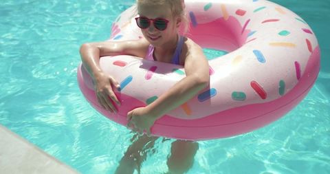 Little girl floating on pink donut pool tube wearing sunglasses enjoying sunny summer