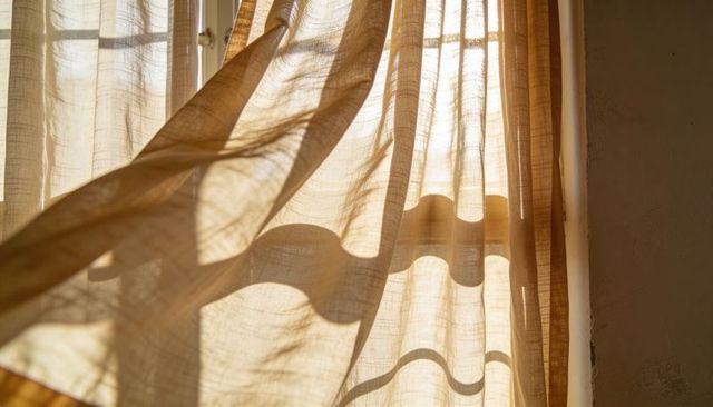 Billowing Sheer Beige Curtains Casting Warm Sunlight Shadows on Textured Plaster Wall