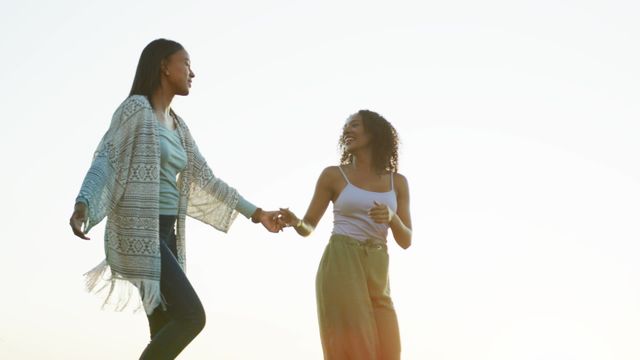 Joyful biracial couple enjoying a moment together by holding hands and dancing outdoors in natural light. Perfect for themes of love, inclusivity, happiness, and lifestyle. Suitable for advertisements, blog posts, social media campaigns, and articles focusing on relationships, diversity, and well-being.