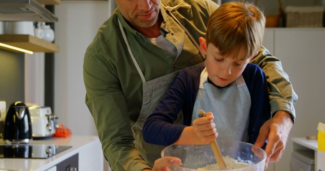 Father helping son mix ingredients in large bowl, teaching baking skills, emphasizing family bonding and teamwork. Suitable for articles on parenting, cooking with family, or promoting family activities.
