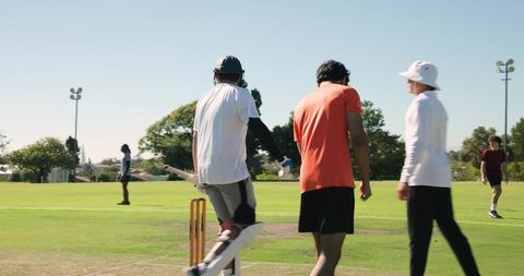 Fast bowler delivering ball while batsman bracing and fielders watching on sunny cricket oval