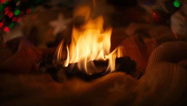 Small warm flame glowing on dark holder amid knit fabric and holiday bokeh lights cozy velvet warmth
