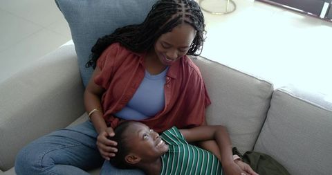 African mother cradling daughter head on sofa, sharing warm smile and affection