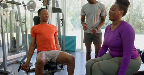 Young couple lifting weights inside gym with personal trainer