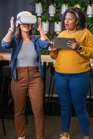 Diverse female coworkers trying virtual reality headset in modern lounge for team training