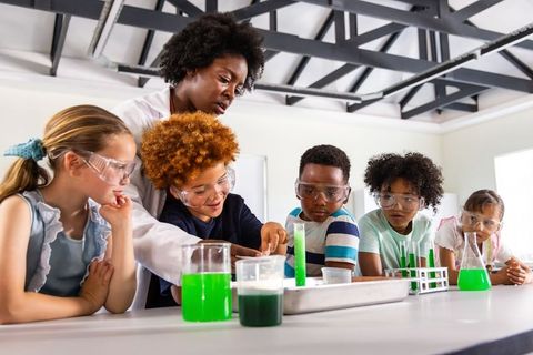Teacher guiding diverse students conducting chemistry experiment with safety goggles