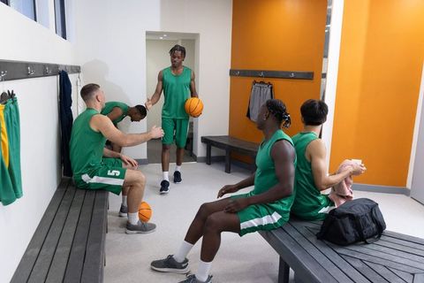 Basketball team preparing in locker room wearing green jerseys showing camaraderie