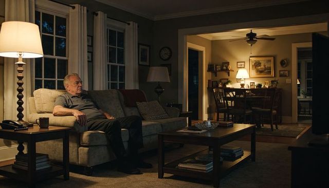 Senior man watching tv on beige sofa in cozy living room at night, warm lamp glow