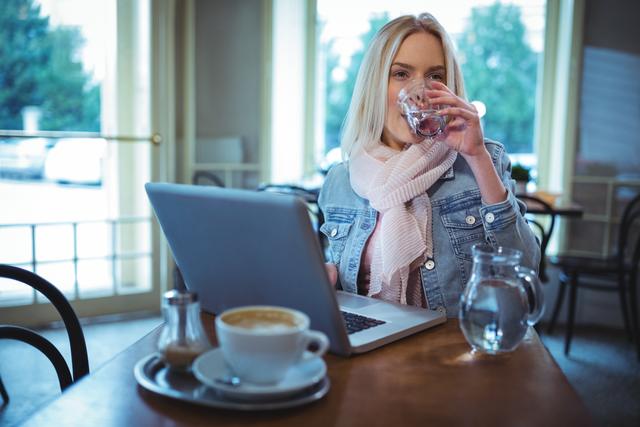 Woman having a glass of water while using laptop in cafÃ©