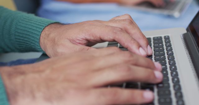 Close-up view of a man typing on laptop keyboard, showcasing work in a casual setting. Perfect for use in articles related to productivity, remote work, technology use, office tasks, and professional activities.