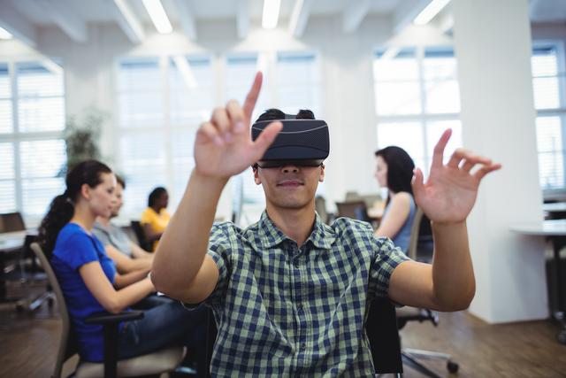 Man using virtual reality headset in modern office environment. Colleagues working in background. Ideal for illustrating concepts of technology integration in workplace, future of work, and digital innovation.