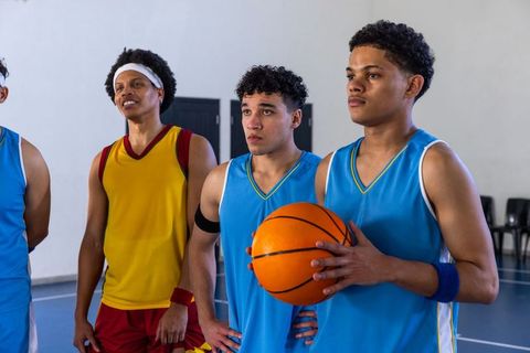 Diverse Male Teammates Posing with Basketball in Gym