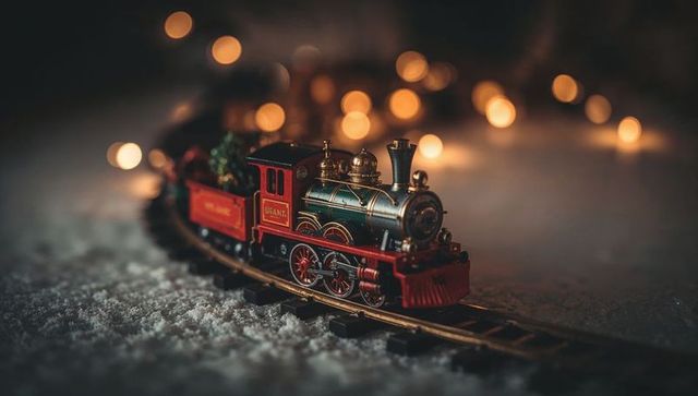 Vintage mini steam locomotive on snowy track with warm bokeh holiday lights and tender