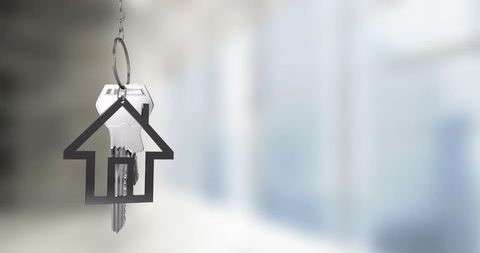 House key hanging on ring with metal house outline keychain over soft blurred office lobby