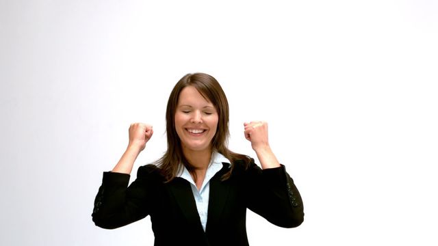 Businesswoman wearing a suit celebrating her success with a joyful expression. Video is perfect for concepts related to corporate achievement, motivation, happiness, workplace success, and positive mindset.