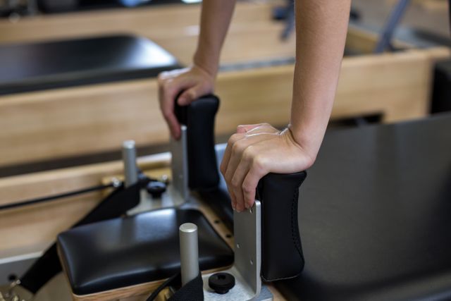 Close-up of a woman's hands gripping the handles of a Pilates reformer machine. Ideal for use in fitness blogs, workout guides, and health-related articles to illustrate Pilates exercises and equipment.
