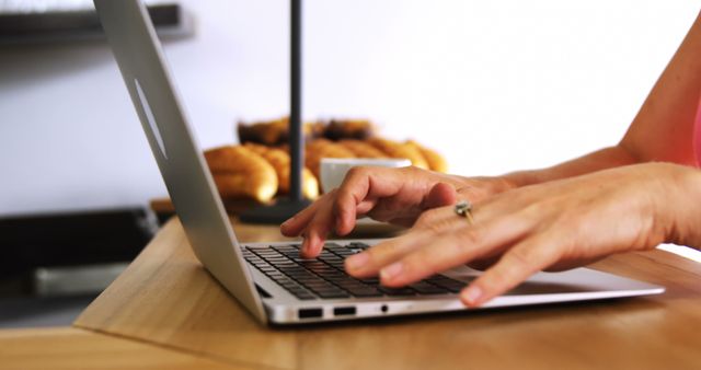 A person is working on a laptop at a wooden table, with a plate of croissants and a cup of coffee nearby, with copy space. Capturing a moment of productivity, the image reflects a comfortable work-from-home environment or a casual office setting.