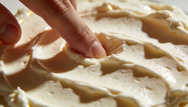 Finger pressing creamy buttercream icing creating dent and swirl texture in closeup