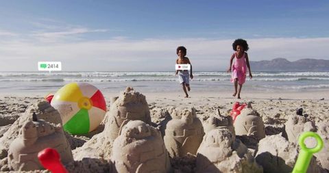 Children racing toward sandcastles on sunny beach with colorful beach ball