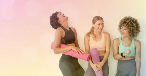 Women laughing holding pink purple yoga mats sharing camaraderie and active wellness