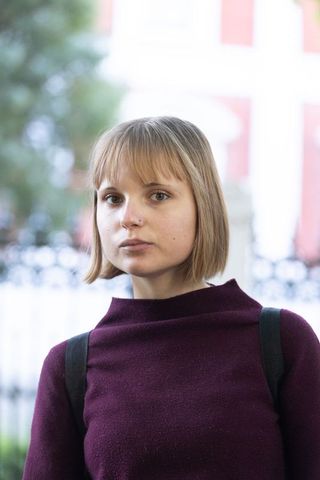 Contemporary young woman portrait wearing maroon sweater, nose stud and backpack in city