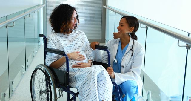 Doctor assisting and talking with a female patient in a wheelchair. Useful for healthcare, patient care, and medical professionalism themes showing compassion and support in a hospital environment.