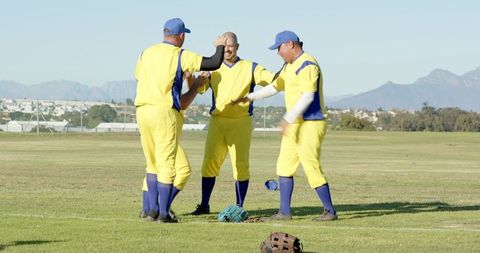 Yellow uniform baseball team cheering and celebrating victory on sunny grass field
