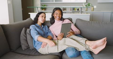 Two Women Using Tablet on Sofa in Bright Modern Home