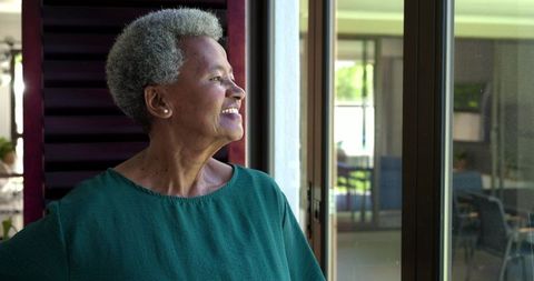 Senior african american woman gazing through sliding glass door feeling serene at home