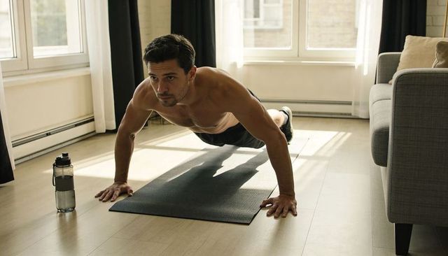 Shirtless man performing push-up on mat in sunlit living room for home fitness routine