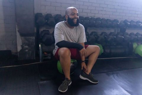 Smiling african american man resting on medicine ball in industrial gym interior