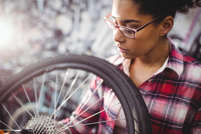 Young female mechanic examining a bicycle wheel in a workshop, focusing on maintenance and repairs. Ideal for use in articles or advertisements about mechanical skills, cycling, female empowerment in male-dominated fields, transportation, and repair services.